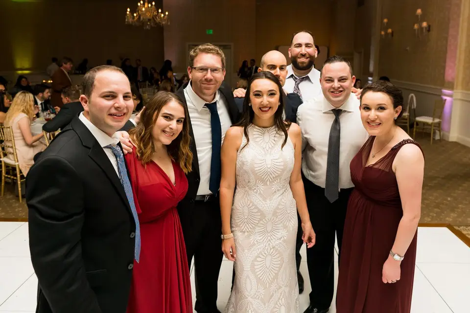 Allison and Brandon posing with five friends in formal wear on the dance floor at their reception