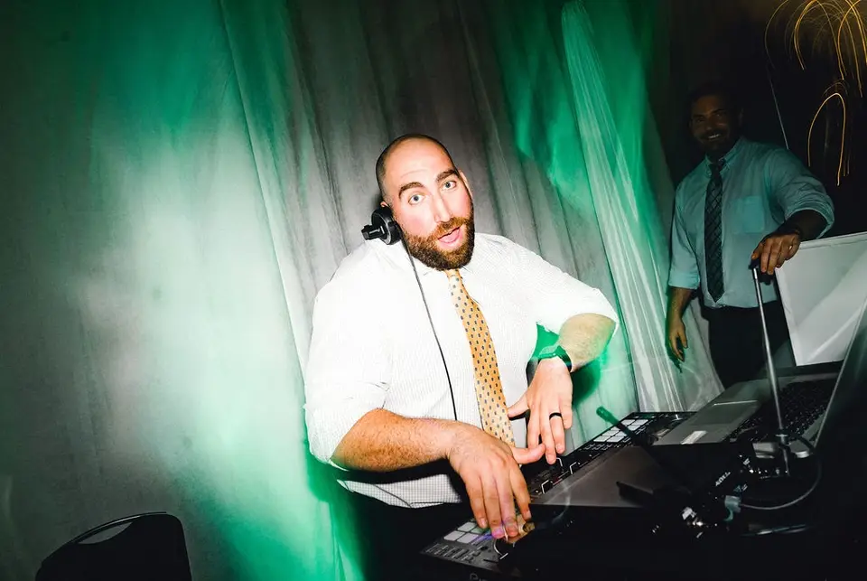 DJ with headphones and a beard working at his controller under green lighting