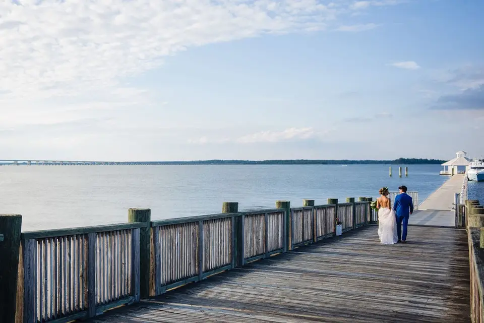 Bride and groom walking away along a wooden boardwalk beside the water