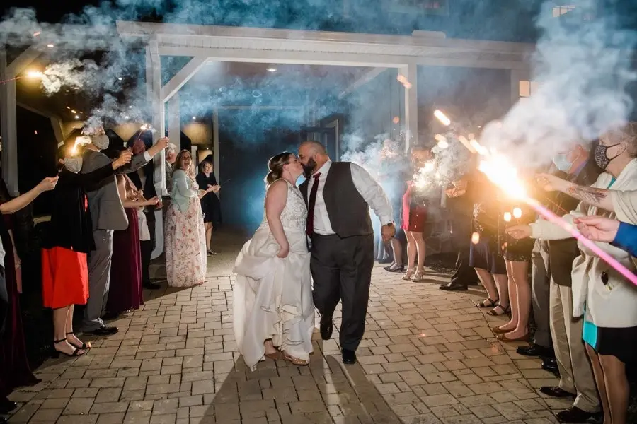 Bride and groom walking through a sparkler send-off as guests line a brick path at night