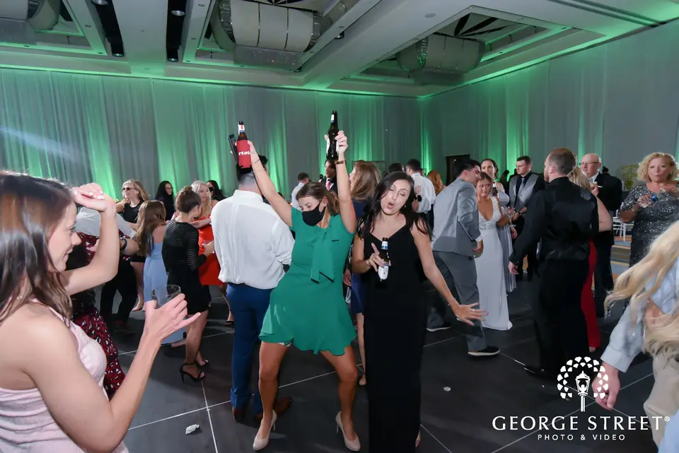 Guests dancing and holding bottles on a dark dance floor with green uplighting