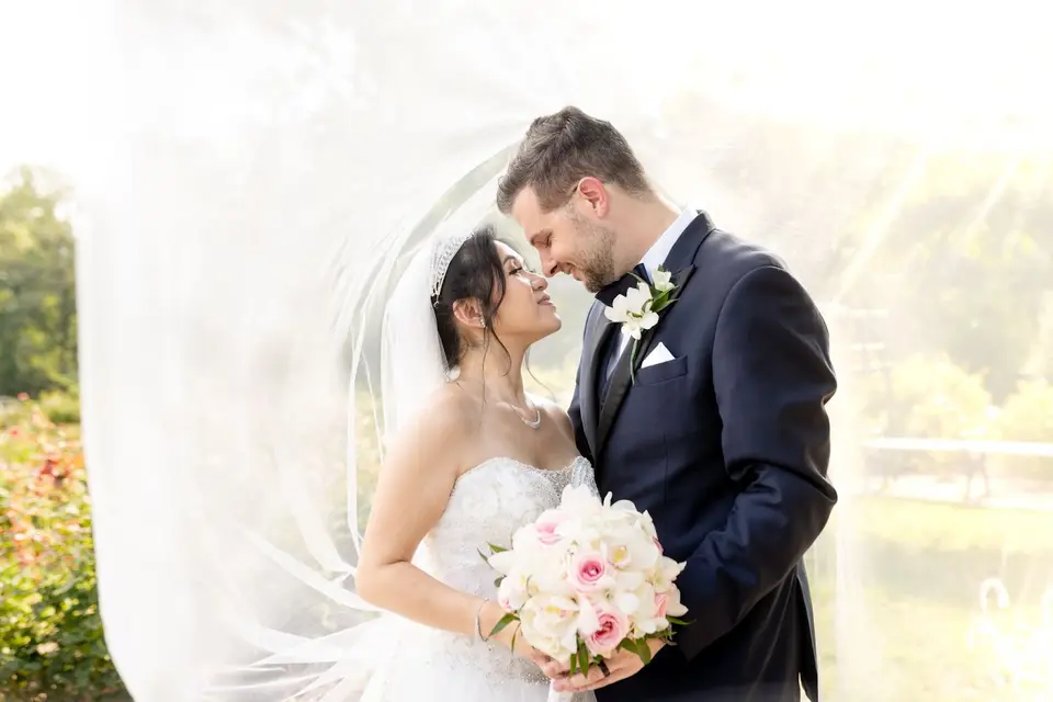 Bride and groom embracing under her flowing veil, holding a pink and white bouquet