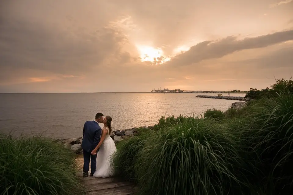 Bride and groom kiss on a wooden path above the water at sunset