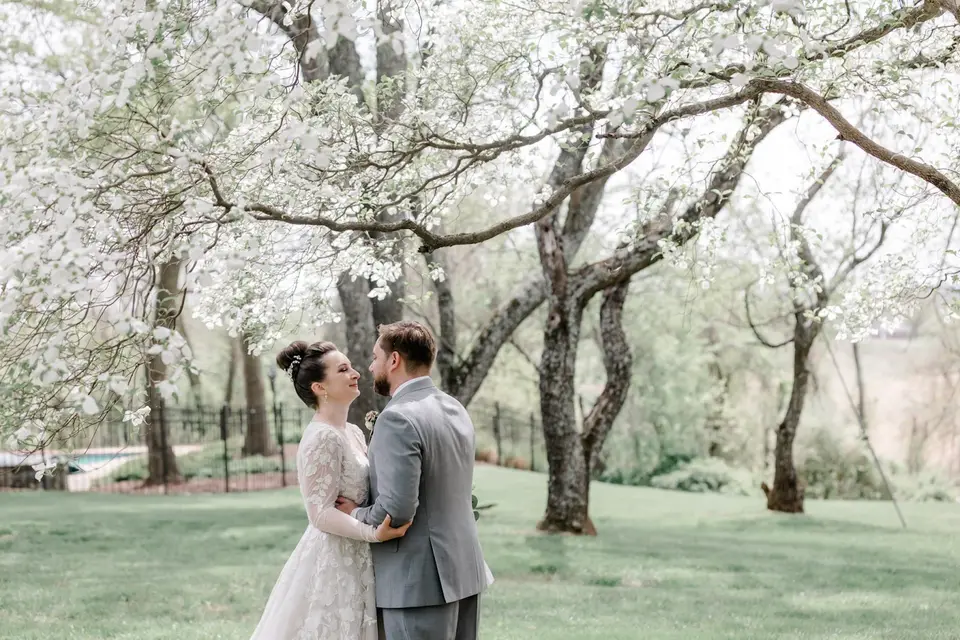 Bride and groom embrace and smile at each other under blooming white dogwood trees