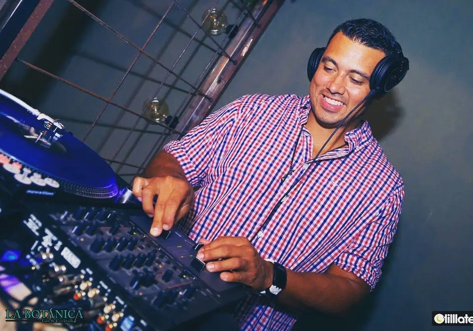 DJ smiling and wearing headphones while working a mixer next to a turntable